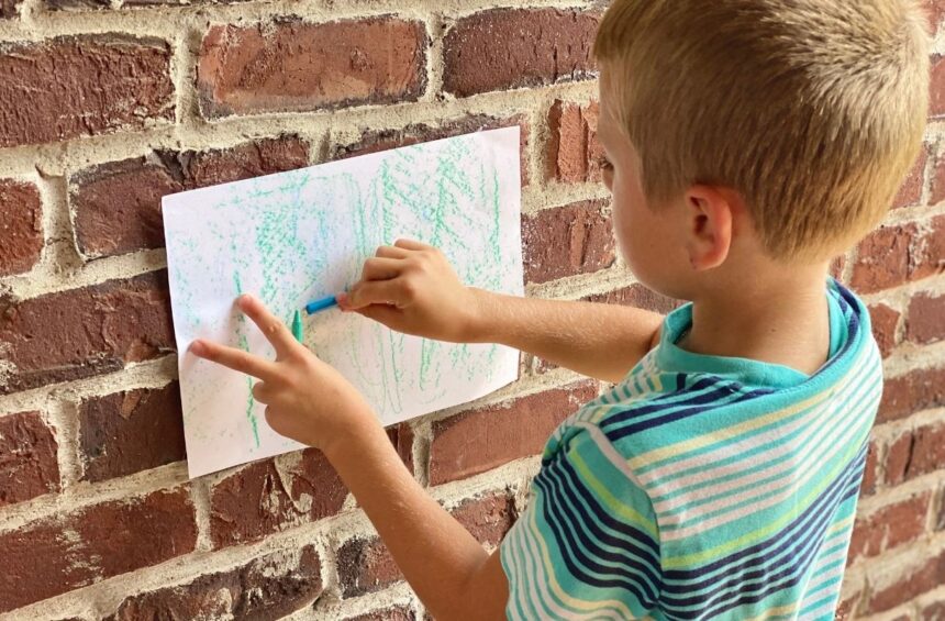 Child exploring texture by rubbing crayons over paper on different surfaces