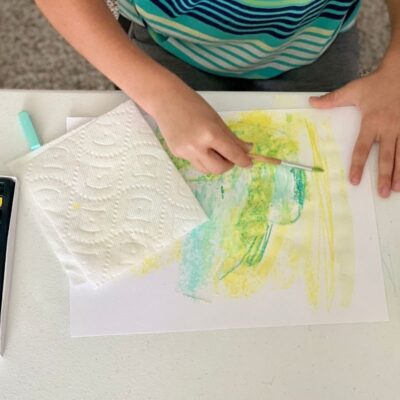 Child makes marks with chalk pastel and uses paint brush and water over it to fill paper