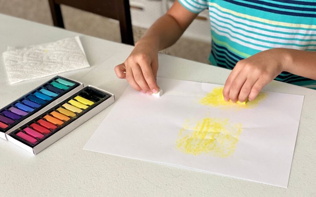 Child makes marks using chalk to fill paper