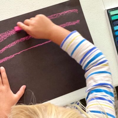 Child making marks with chalk pastels on black paper