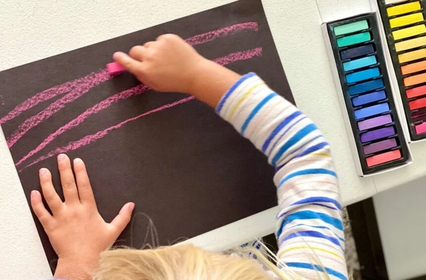 Child making marks with chalk pastels on black paper