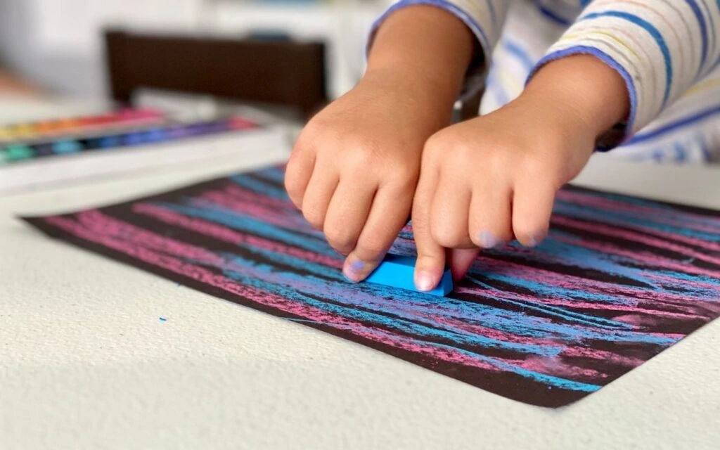Child holding soft pastels and pressing to make marks on black paper