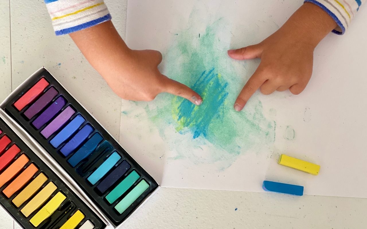 Child using fingers to blend soft pastel on paper