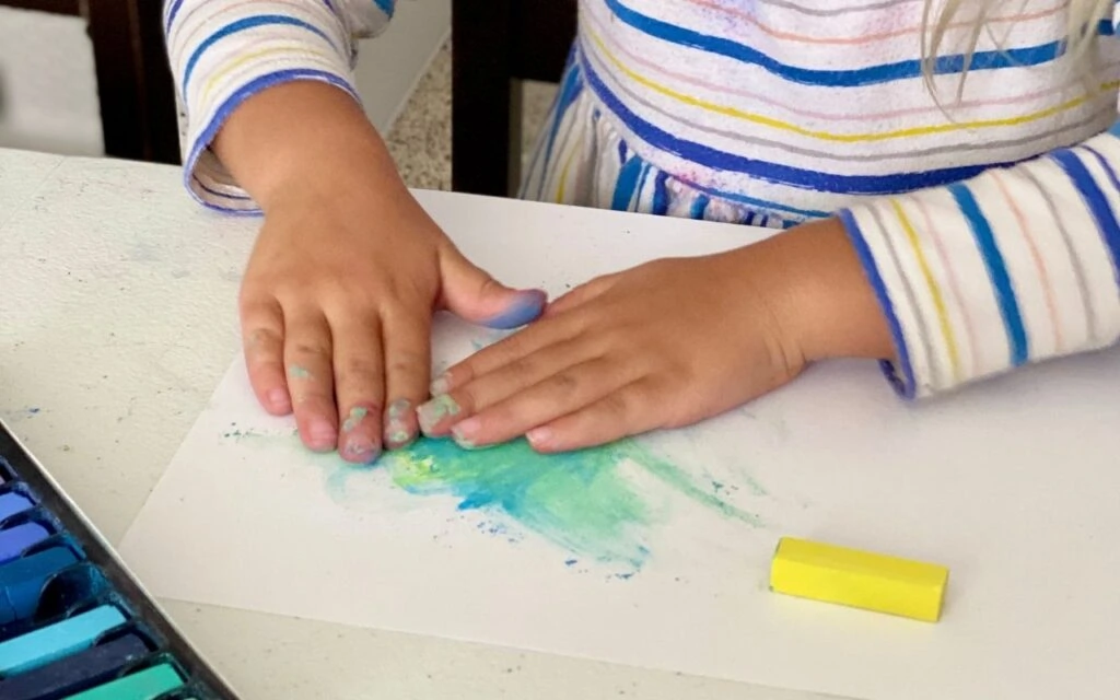Child uses both hands to blend the soft pastels on paper