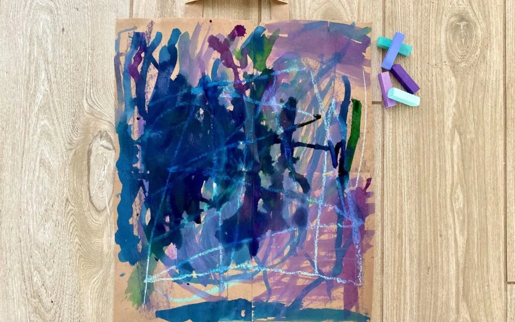 Child drawing chalk on brown paper bag and painting over it with water color
