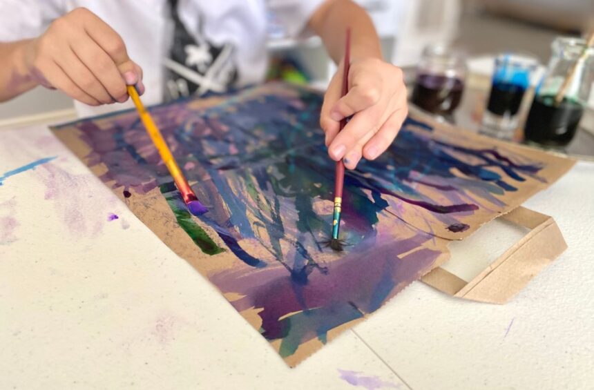 Child drawing chalk on brown paper bag and painting over it with water color