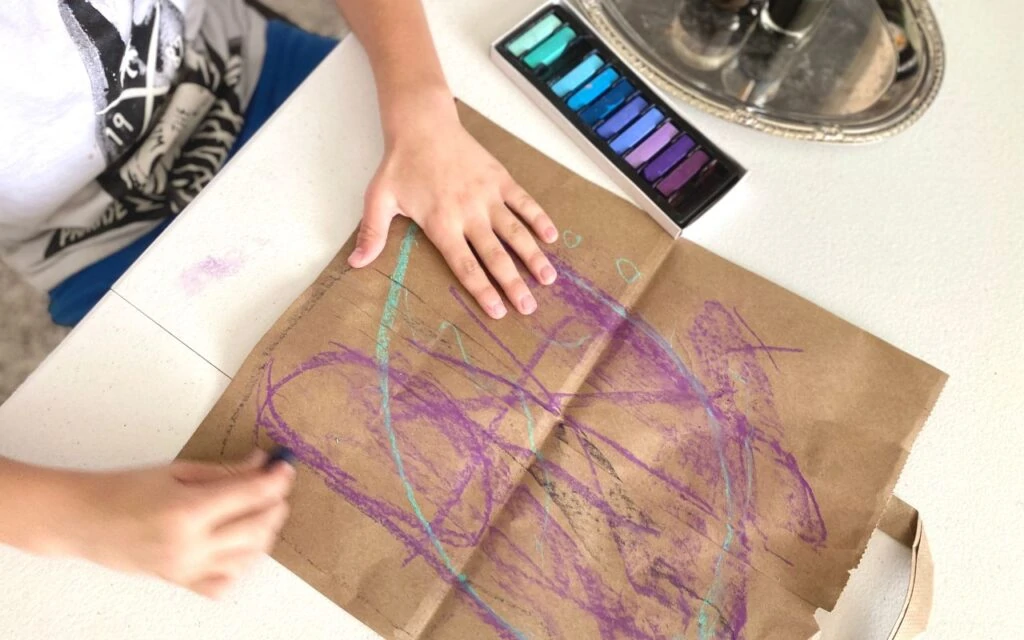 Child drawing with chalk on brown paper bag