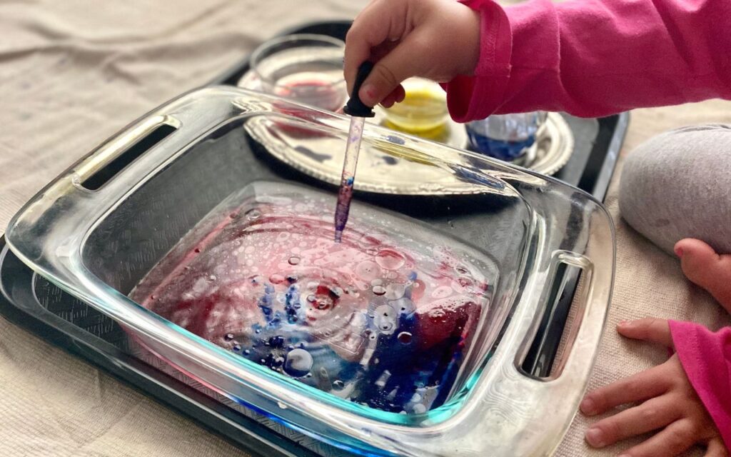 Child adding water color droplets to pan of oil