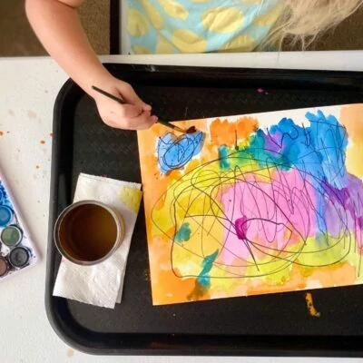 Child painting with water color over sharpies marks