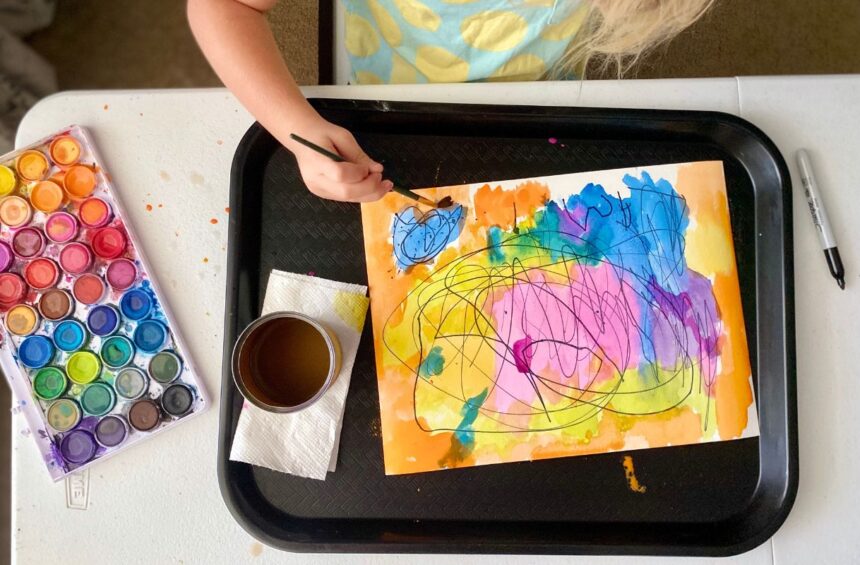 Child painting with water color over sharpies marks