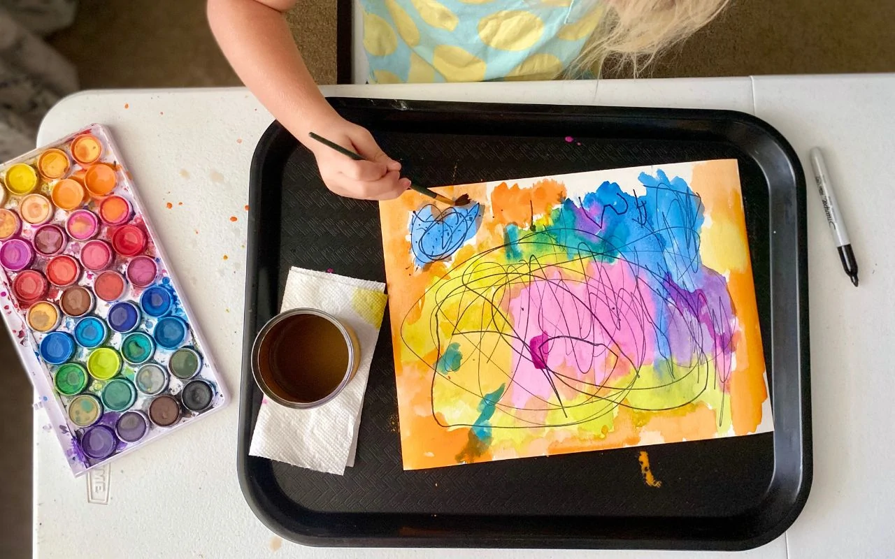 Child painting with water color over sharpies marks