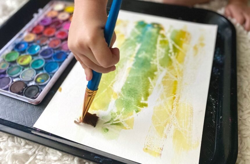 Child painting with water color over candle stick marks