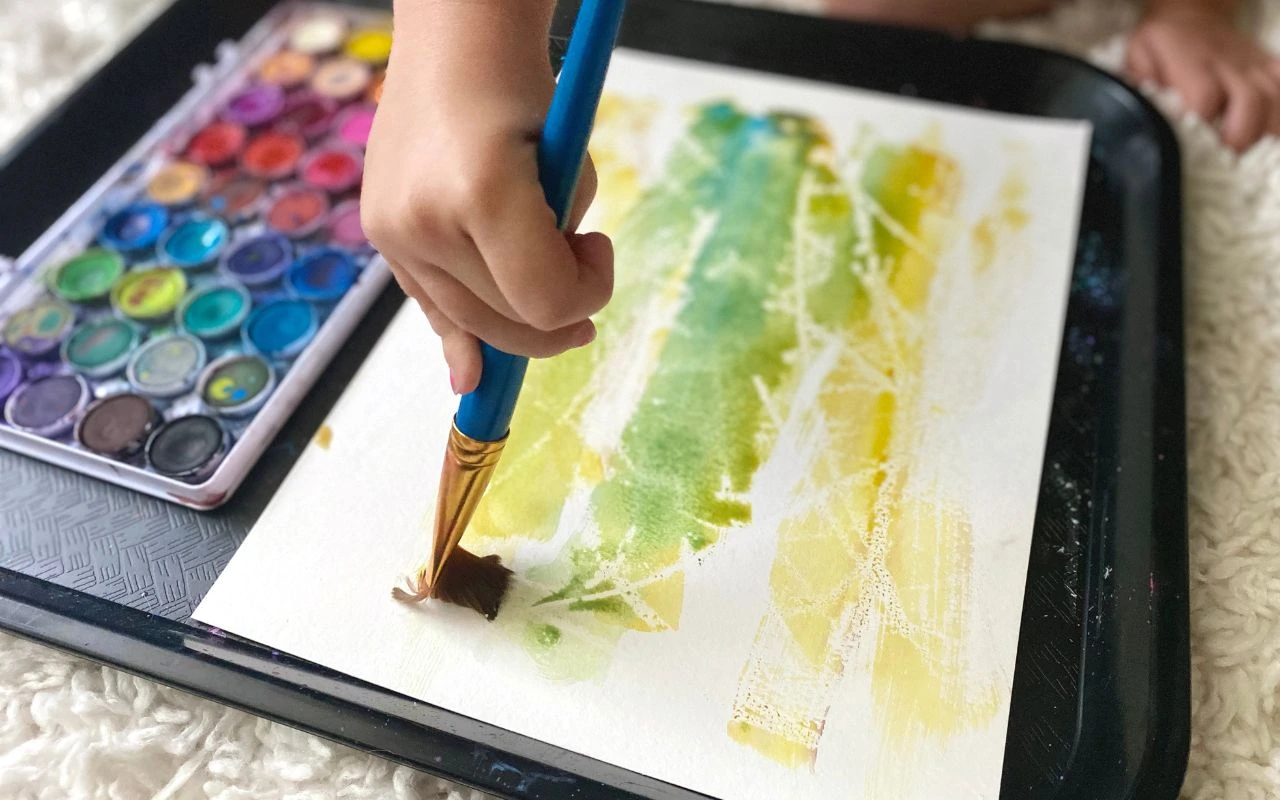 Child painting with water color over candle stick marks