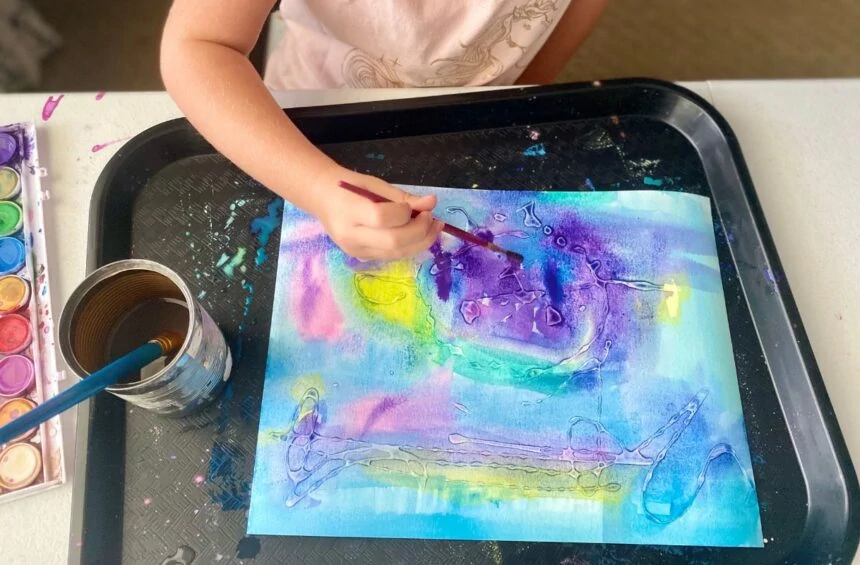 Child painting over dried glue creating a relief painting