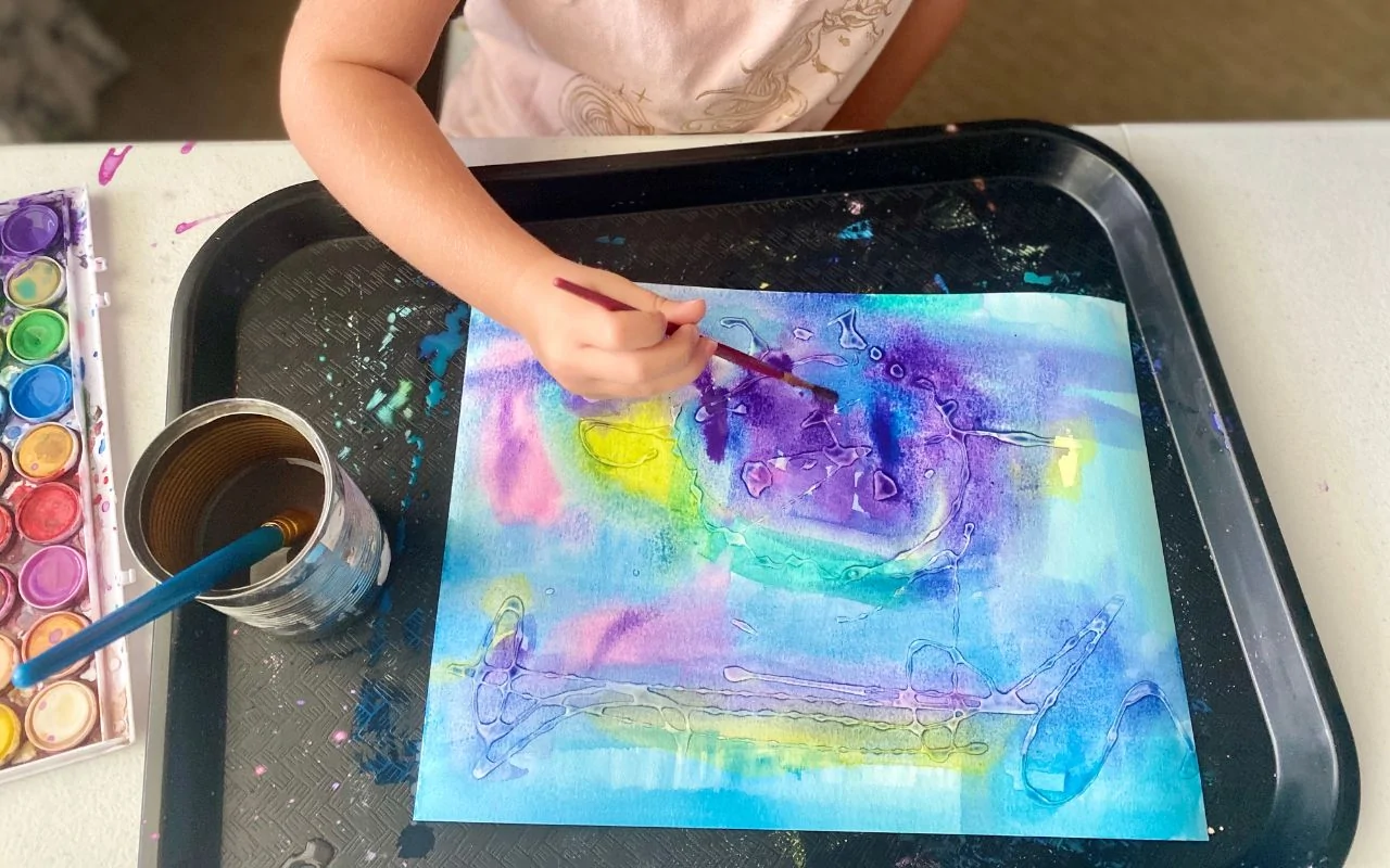 Child painting over dried glue creating a relief painting