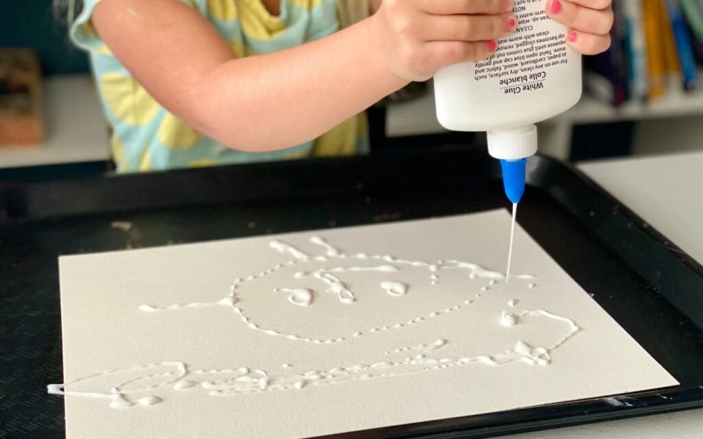 Child making a design with glue on paper