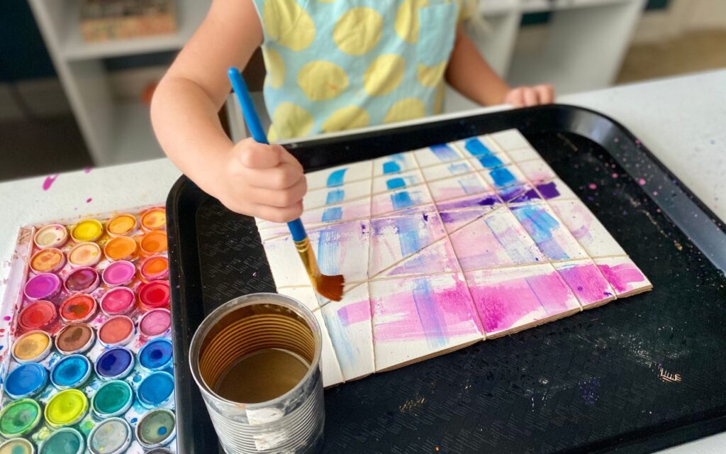 Child painting over rubber band secured to a paper