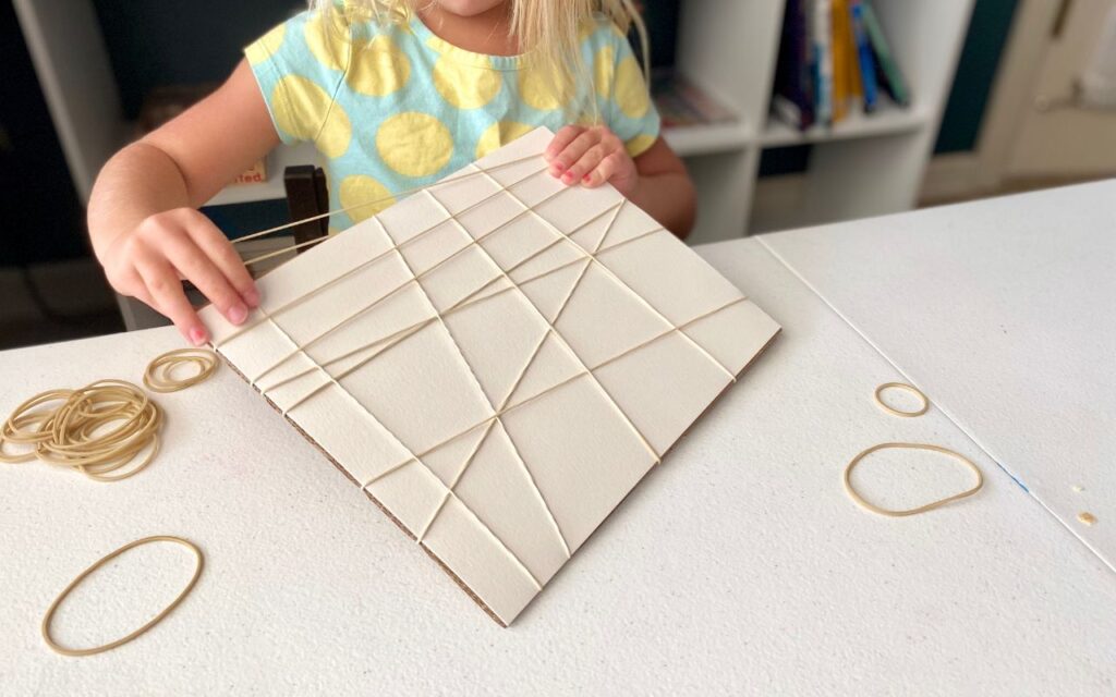 Child placing rubber bands around paper