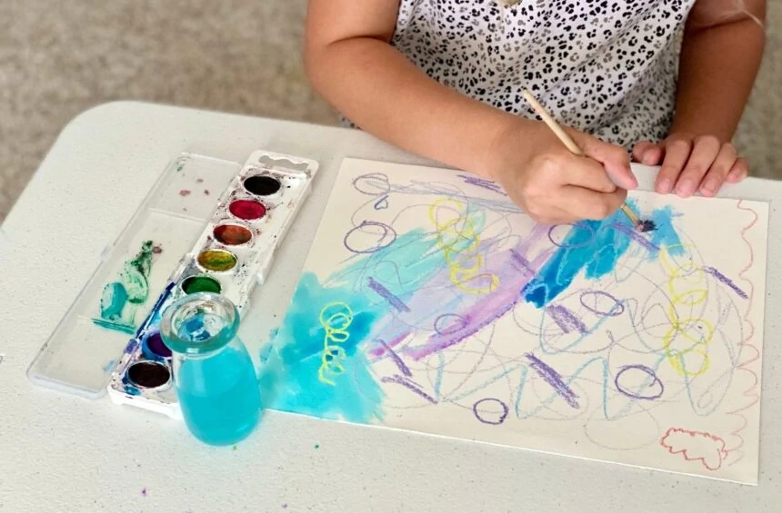 Child makes marks with crayons and paints with watercolor paint over marks