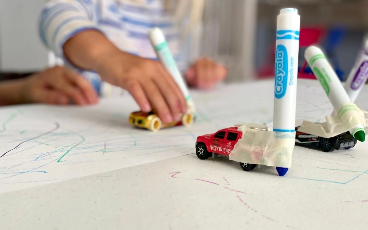 Child holding toy car with a marker taped to it to create marks while moving car