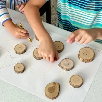 Children drawing marks around wood cookies on paper
