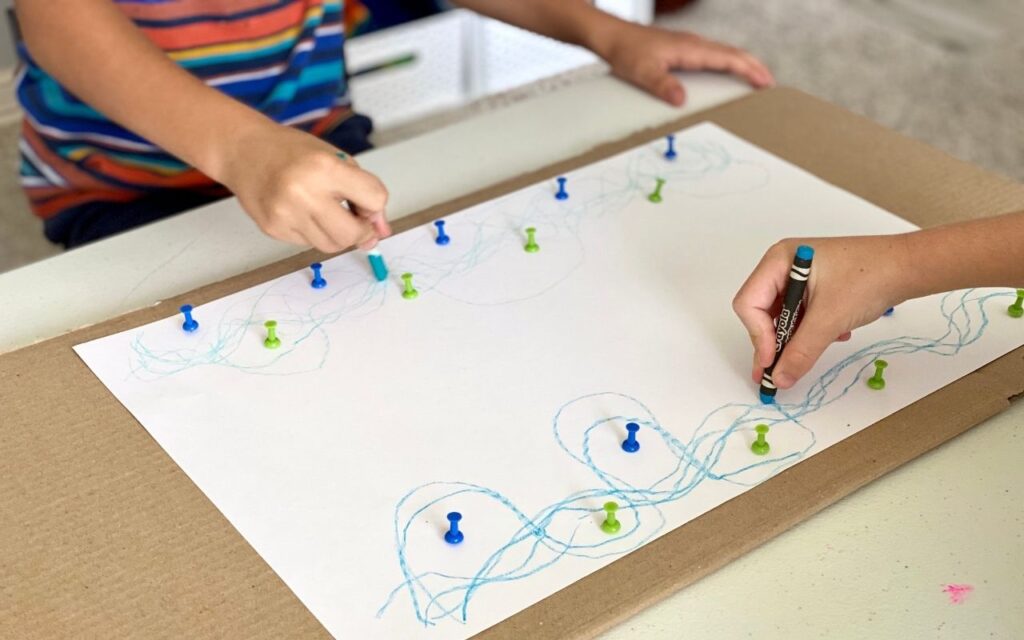 Child making marks around push pins as an obstacle drawing