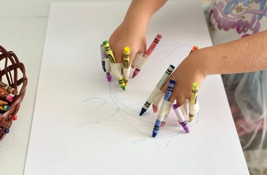 Child drawing on big paper with crayons taped like claws to fingers