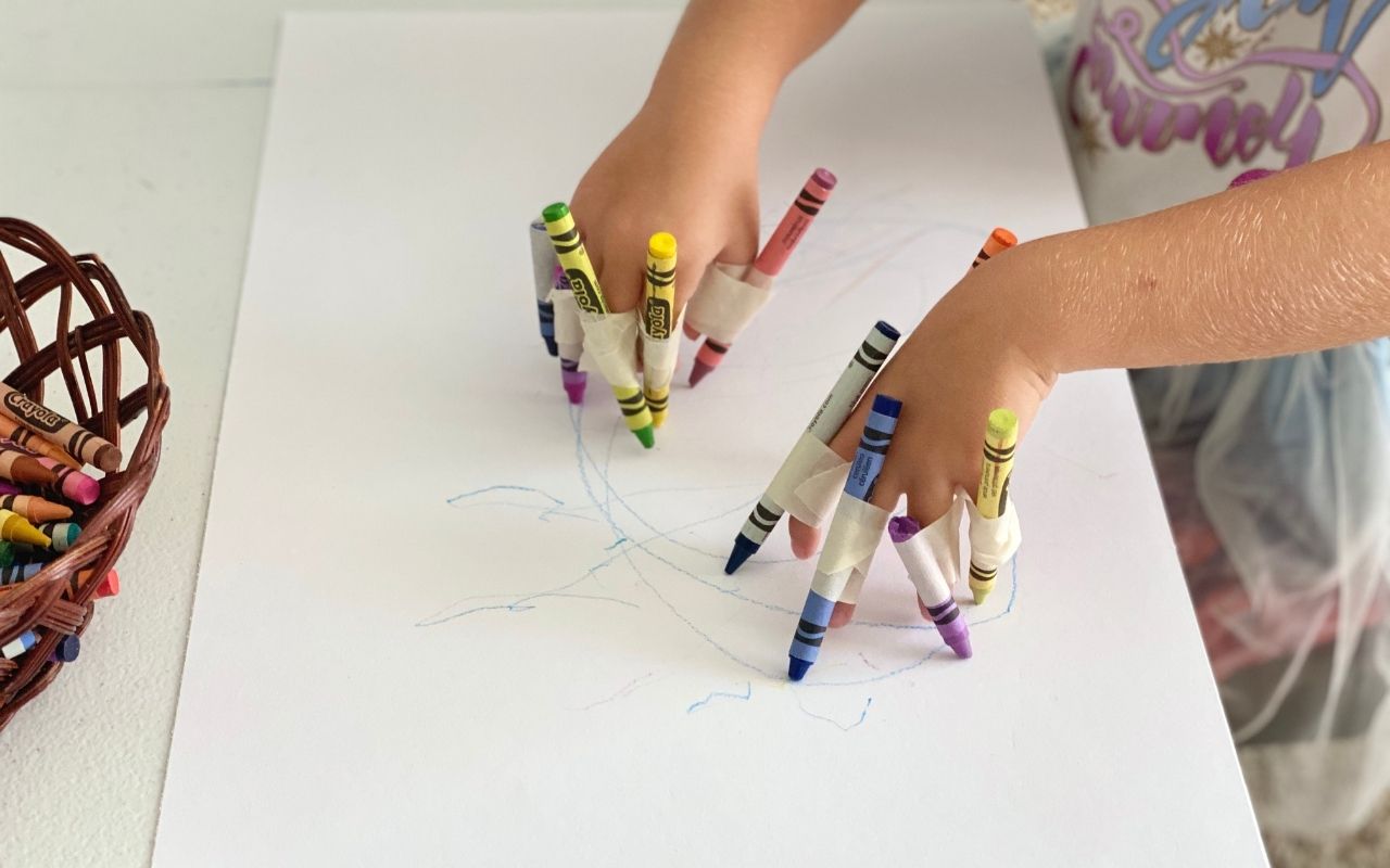Child drawing on big paper with crayons taped like claws to fingers