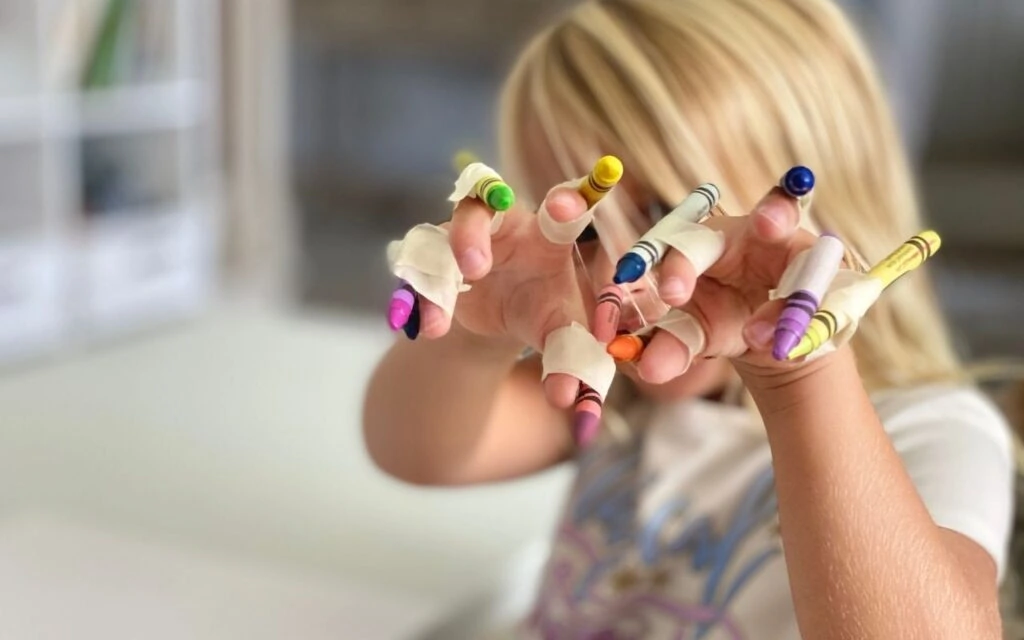 Child showing crayons taped to fingers like claws