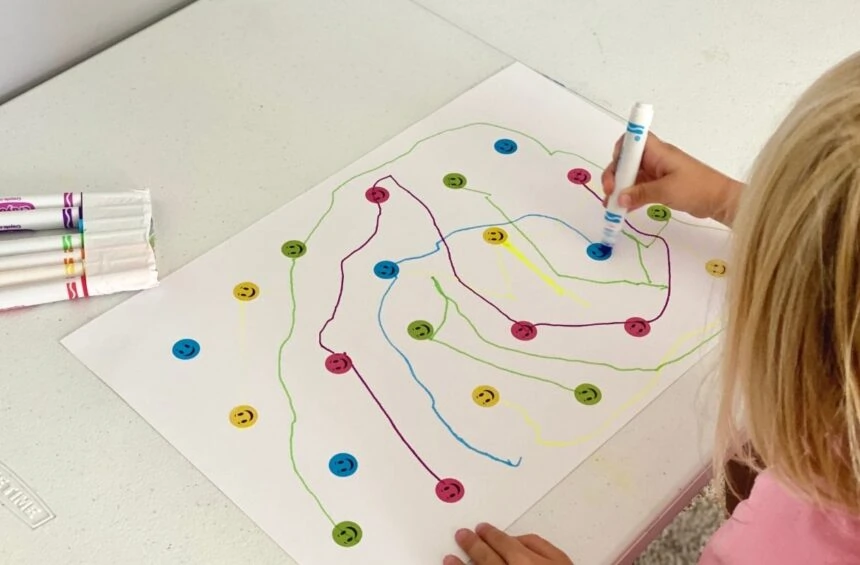 Child sticking colorful stickers on paper and drawing to connect dot to do