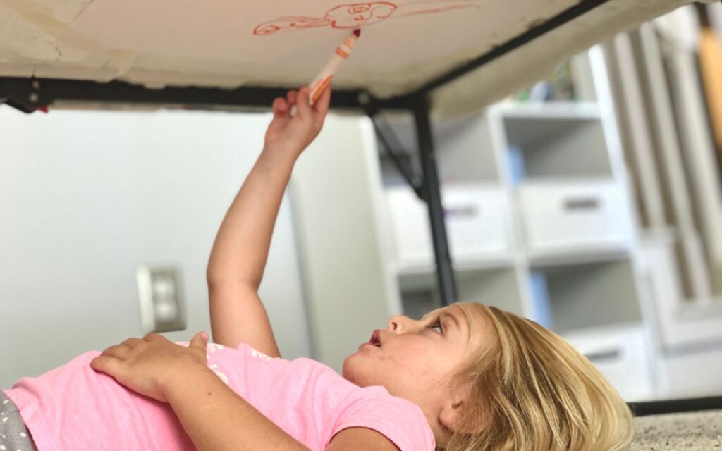 Child drawing under table with paper taped above them