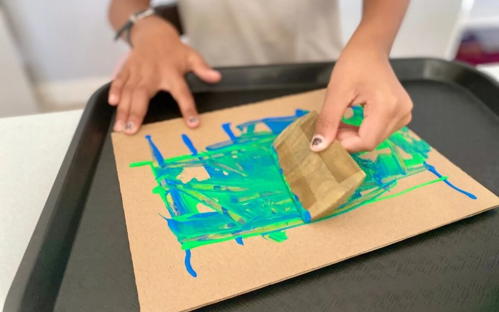 Child painting carboard using a comb