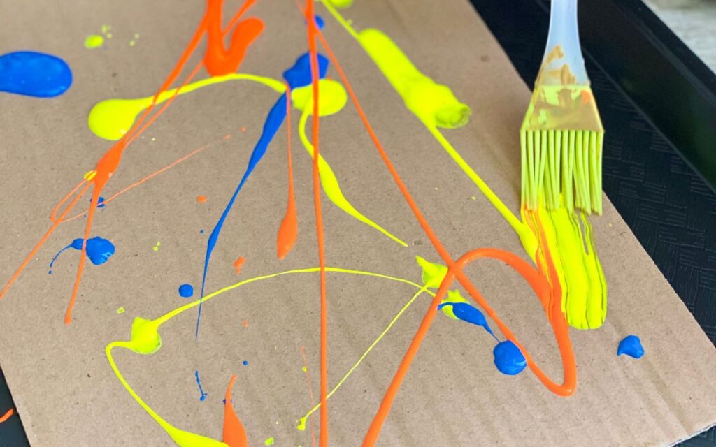 Child uses basting brush to paint on cardboard