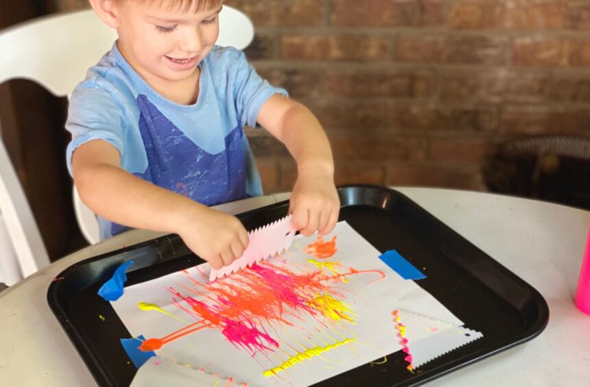 Child uses a cake scraper to spread paint around paper