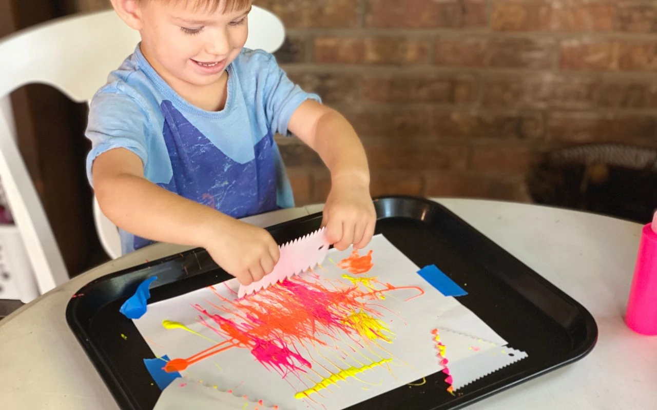 Child uses a cake scraper to spread paint around paper