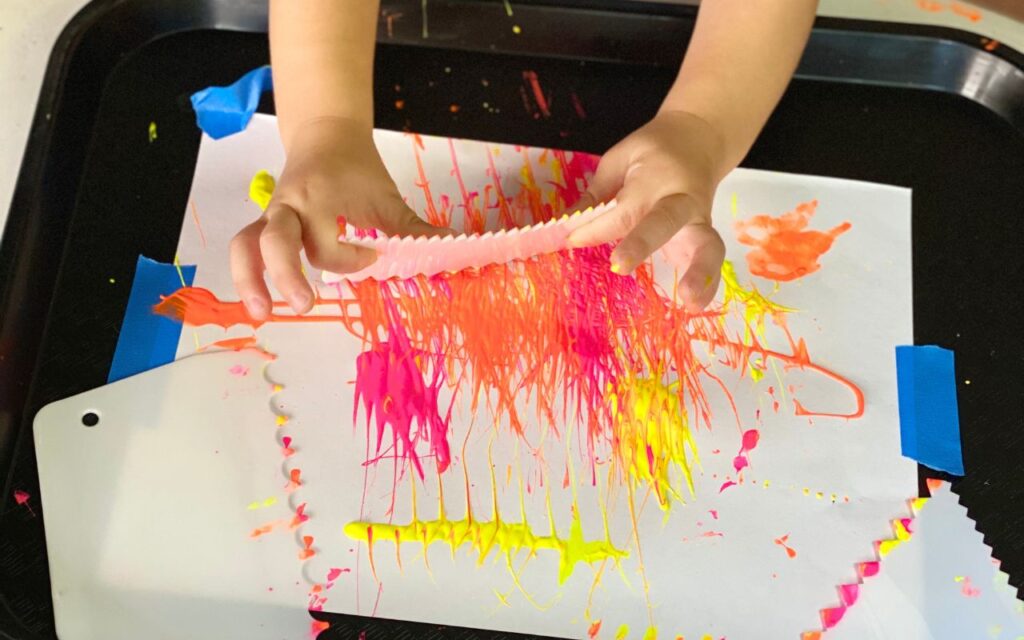 Child uses a cake scraper to spread paint around paper