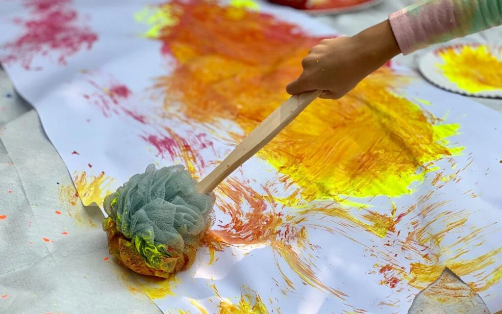 Child using bath pouf while painting on large paper