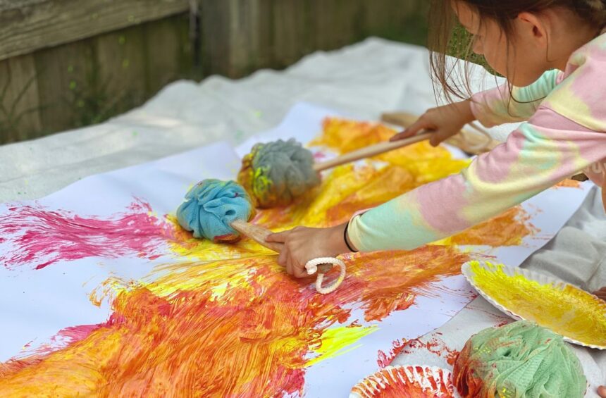 Child using bath pouf while painting on large paper