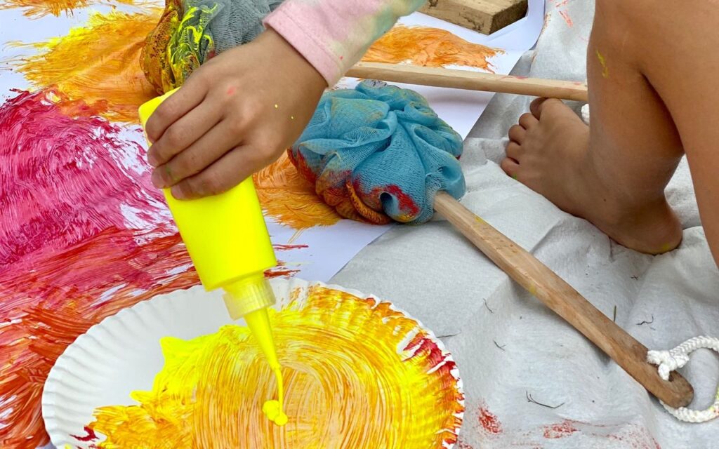 Child using bath pouf while painting on large paper