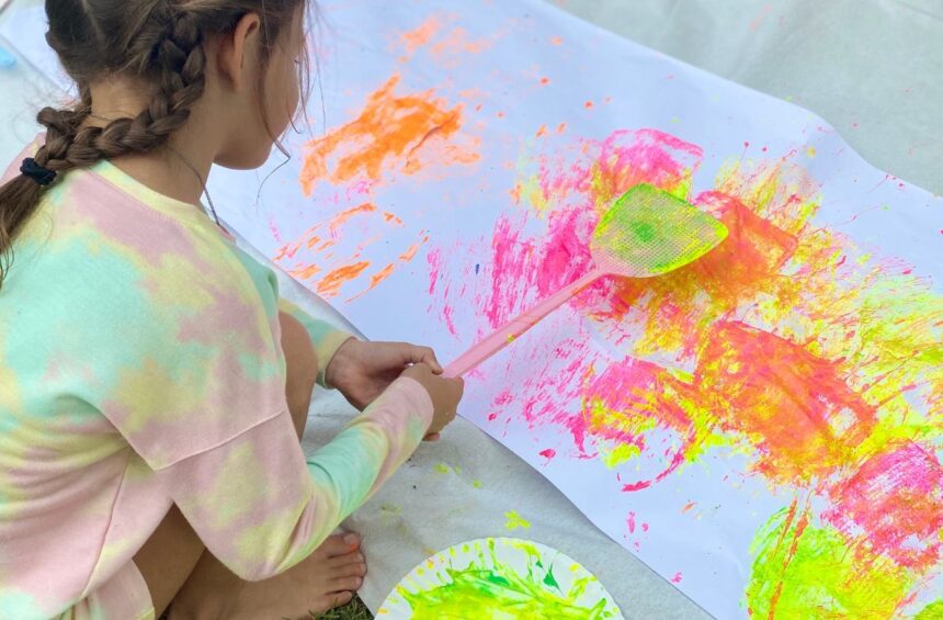 Child swatting paint on large paper with fly swatter