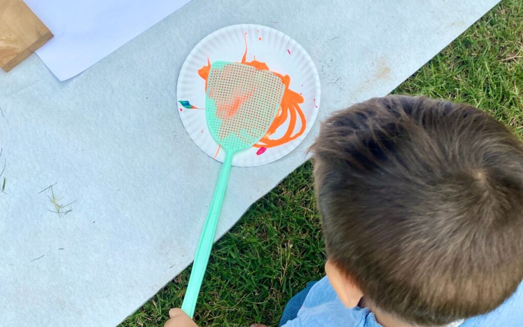 Child swatting paint on large paper with fly swatter