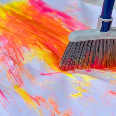 Child using long kitchen broom to swish paint around paper