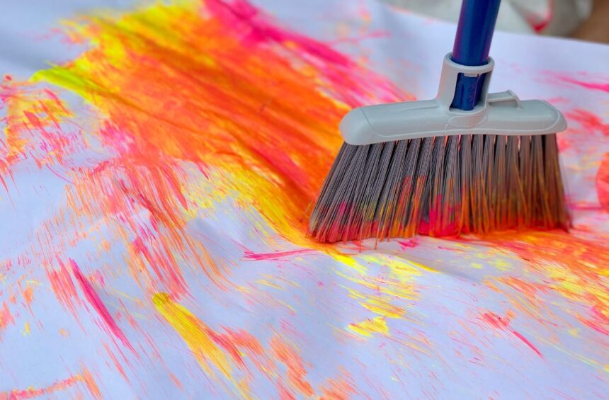 Child using long kitchen broom to swish paint around paper