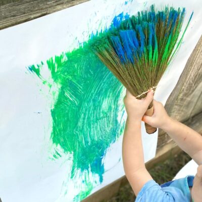 Child uses hand broom to paint on vertical surface