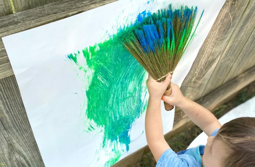 Child uses hand broom to paint on vertical surface