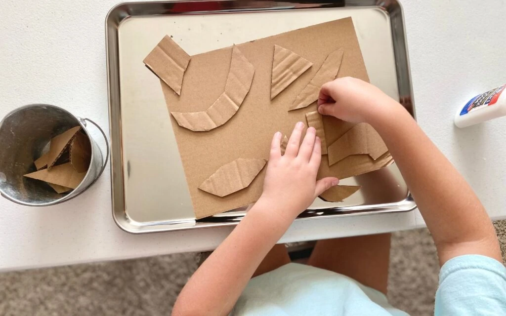 Child cutting and gluing carboard pieces to bigger piece of cardboard