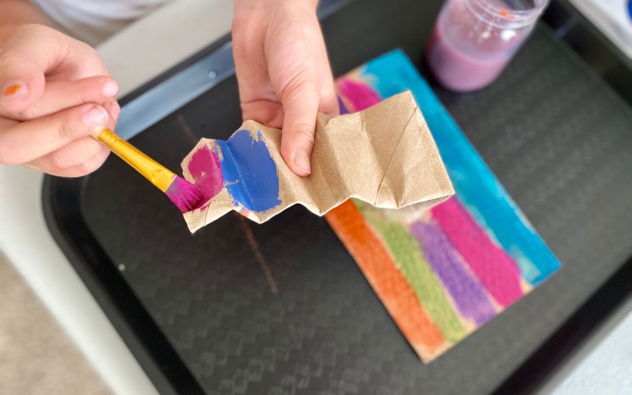 Child painting cardboard tubes glued to a cardboard base