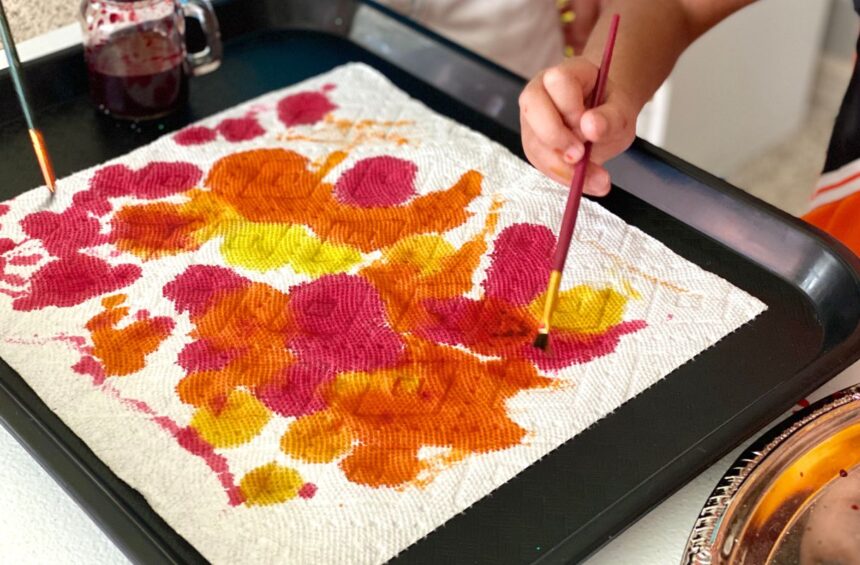 Child spreading liquid water color paint on paper towel