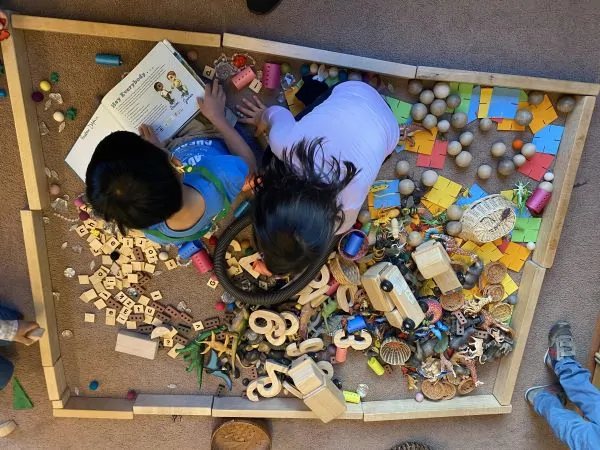 children playing on the floor with a variety of small wooden toys