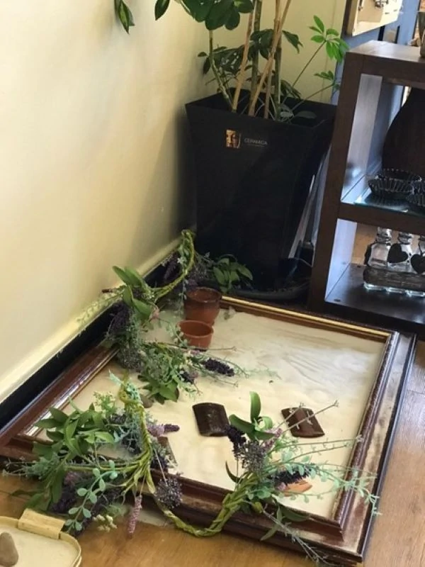 variety of branches with greenery inside of picture frame sand table on the floor